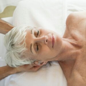 Older woman laying on her back and getting a neck massage while looking relaxed. 
