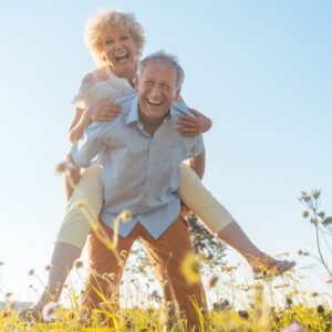 Older man holding a woman on his back, with both of them looking happy. 