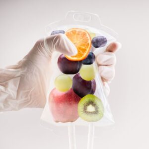 Gloved hand holding on to an IV bag with various fruit in it. 