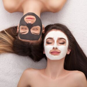 two women laying next to each other, each with a facial mask on. 